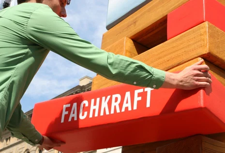 Mann h&auml;lt einen Holzbalken auf dem das Wort Fachkr&auml;fte steht