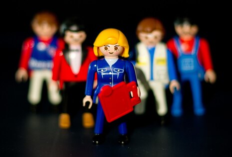 Eine weibliche Playmobil-Figur steht vor mehreren männlichen Figuren.