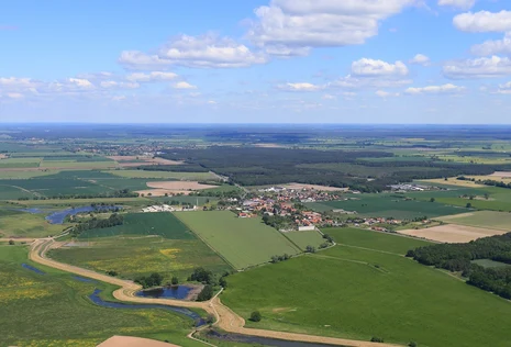  Blick aus der Vogelperspektive auf eine Landschaft mit Feldern, Seen und einem Dorf