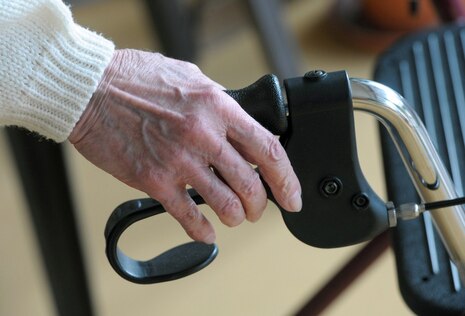 Die Hand einer älteren Person umfasst den Griff eines Rollators.
