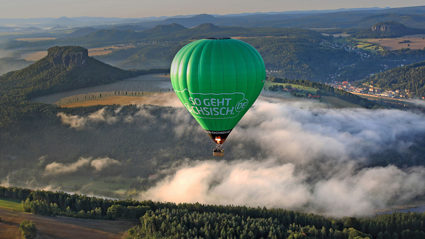 Ein grüner Heißluftballon fährt vor der Kulisse der Sächsischen Schweiz.