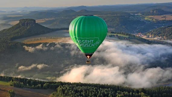 Ein gr&uuml;ner Hei&szlig;luftballon f&auml;hrt vor der Kulisse der S&auml;chsischen Schweiz.