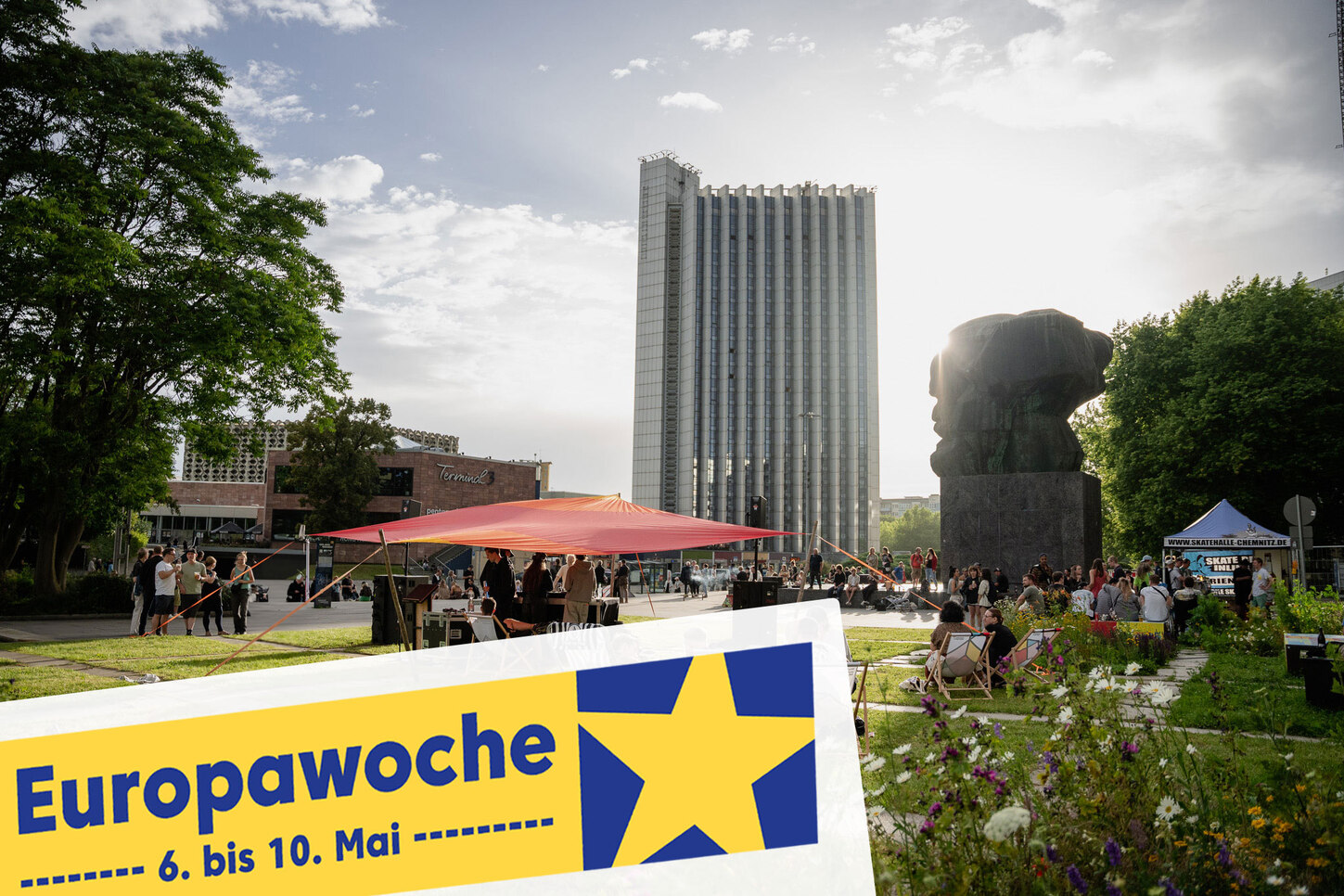 Blick auf ein Hochhaus. Davor eine Wiese mit Strandstühlen auf denen Menschen entspanne.